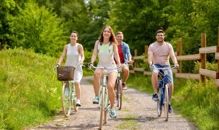 people, leisure and lifestyle concept - happy young friends riding fixed gear bicycles on country road in summer